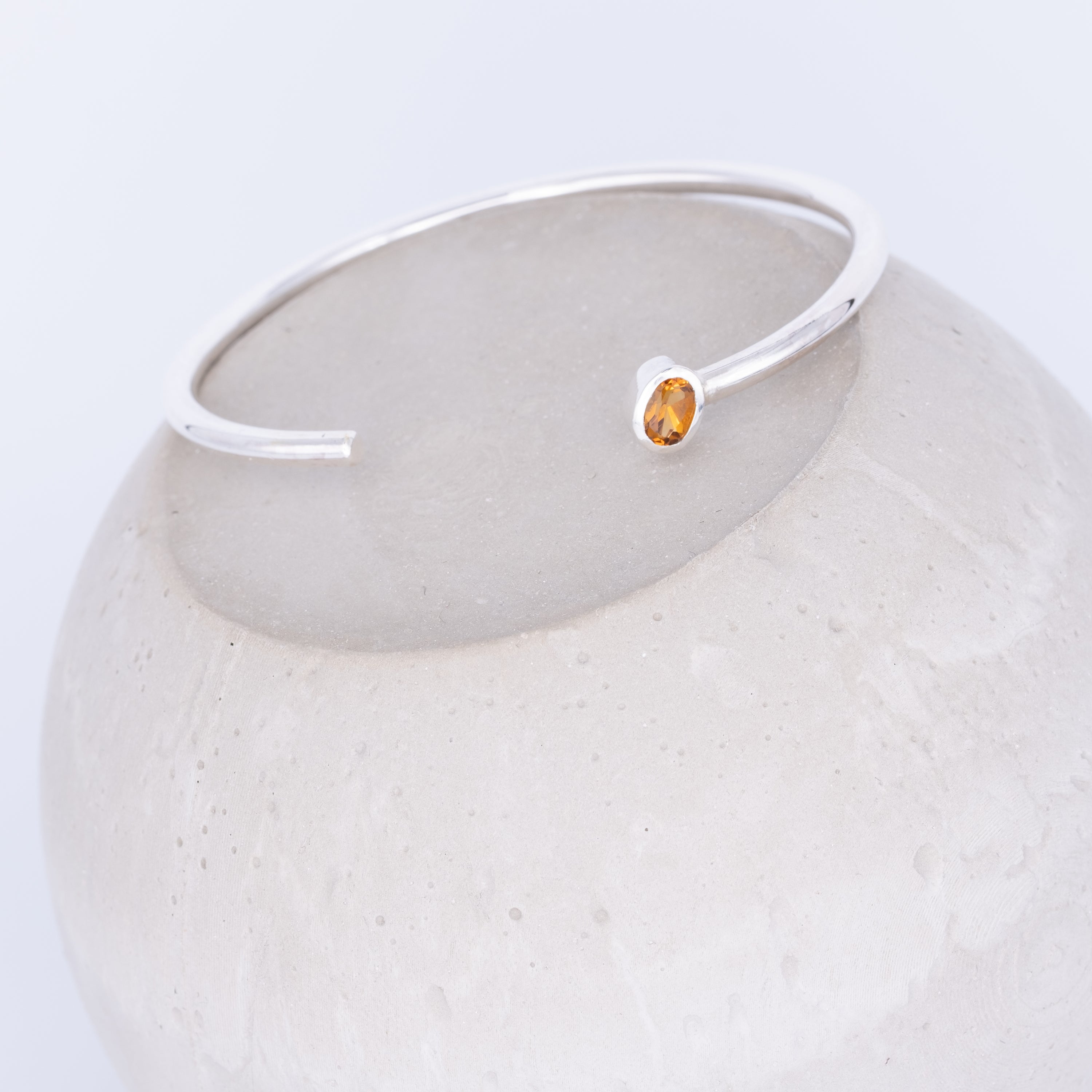 Silver bracelet with a small orange gemstone on a white background