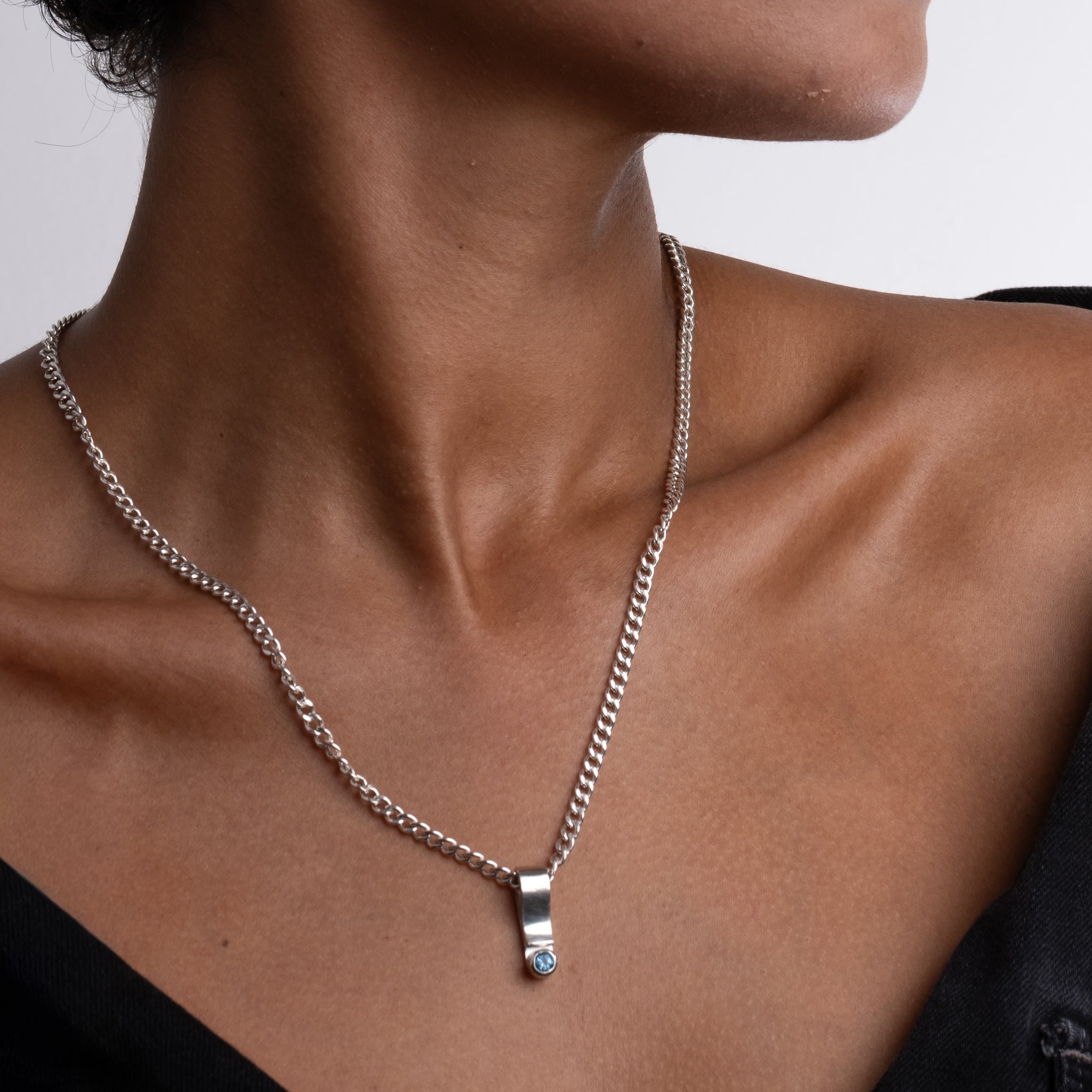 Close-up of a person wearing a silver chain necklace with a small pendant.