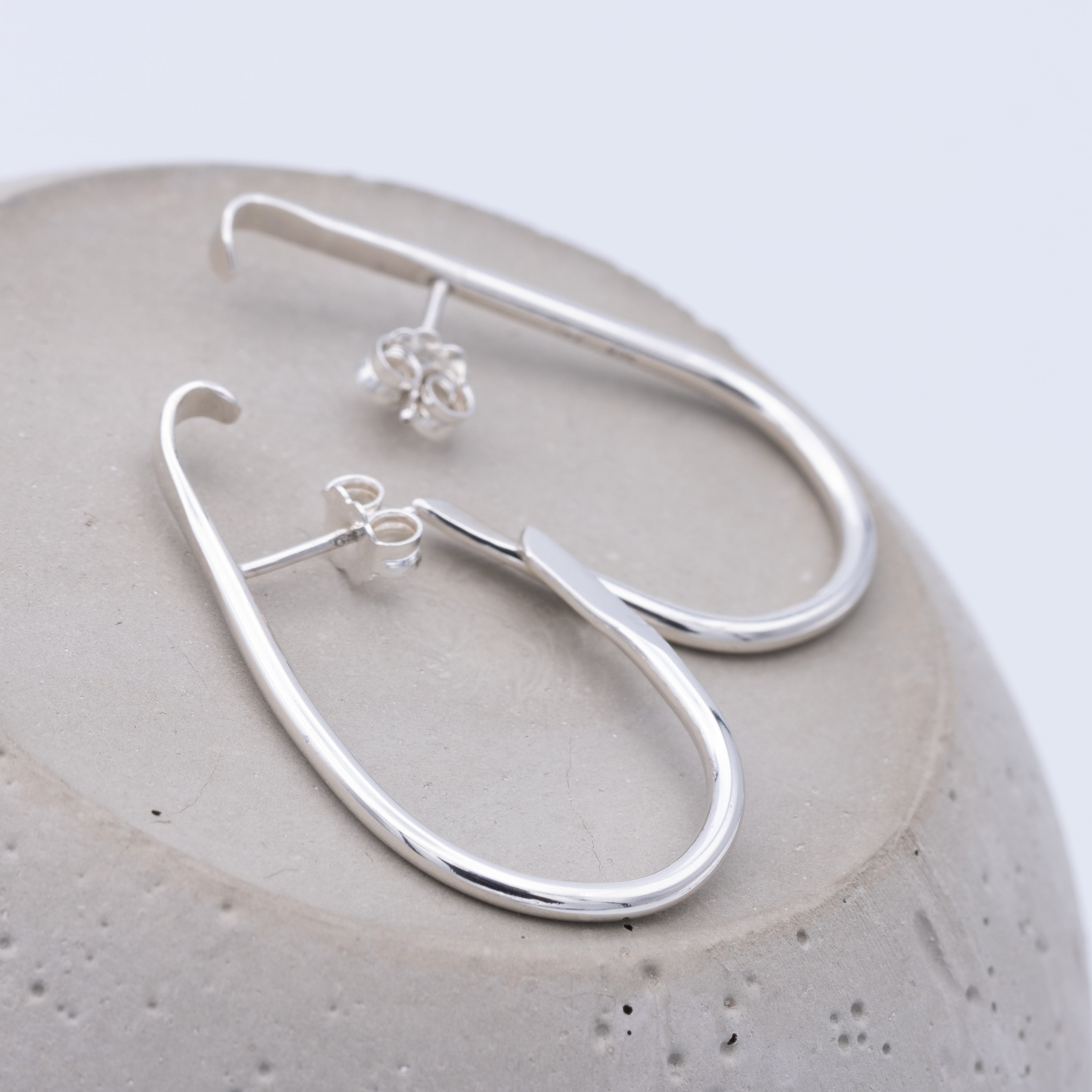 Silver hoop earrings on a textured stone surface
