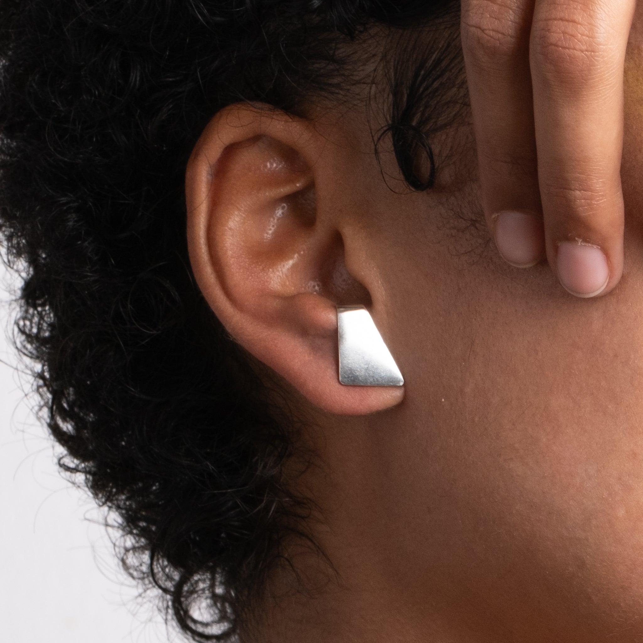 Person wearing a silver triangle earring on a neutral background