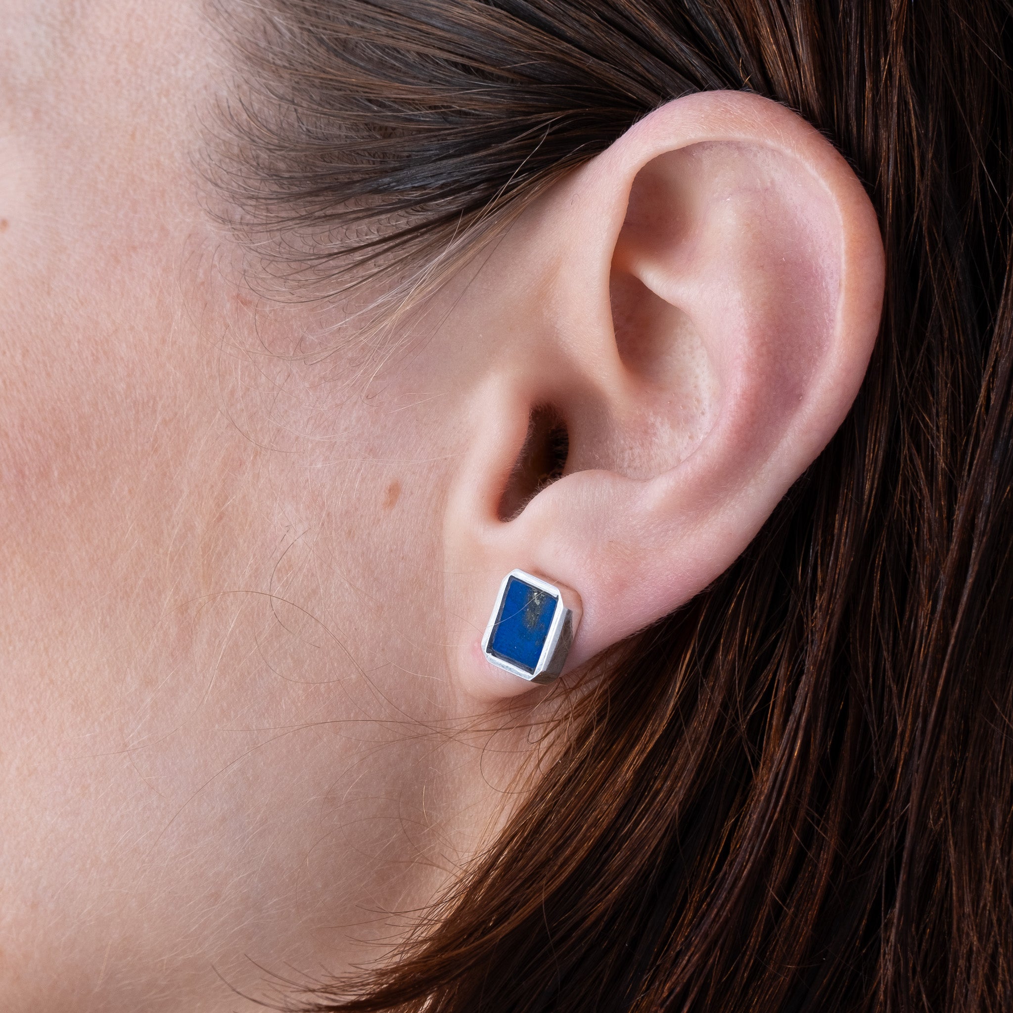 Close-up of an ear wearing a blue and silver earring with lapis lazuli