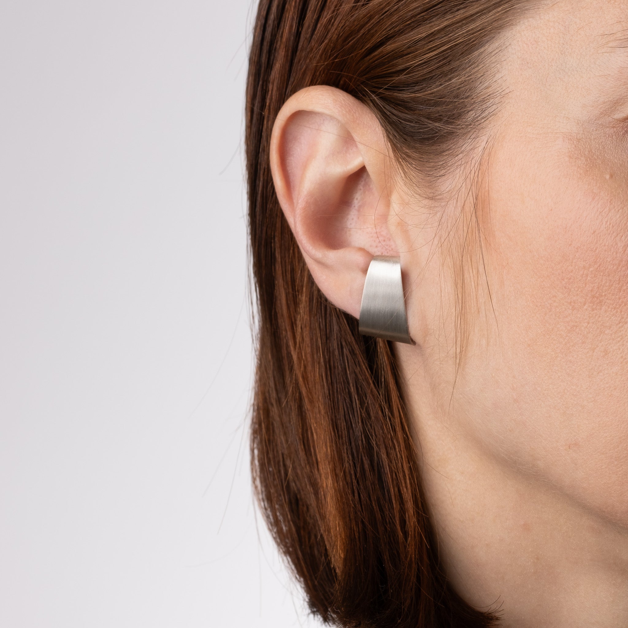 Close-up of a person wearing a silver hoop earring on a plain background