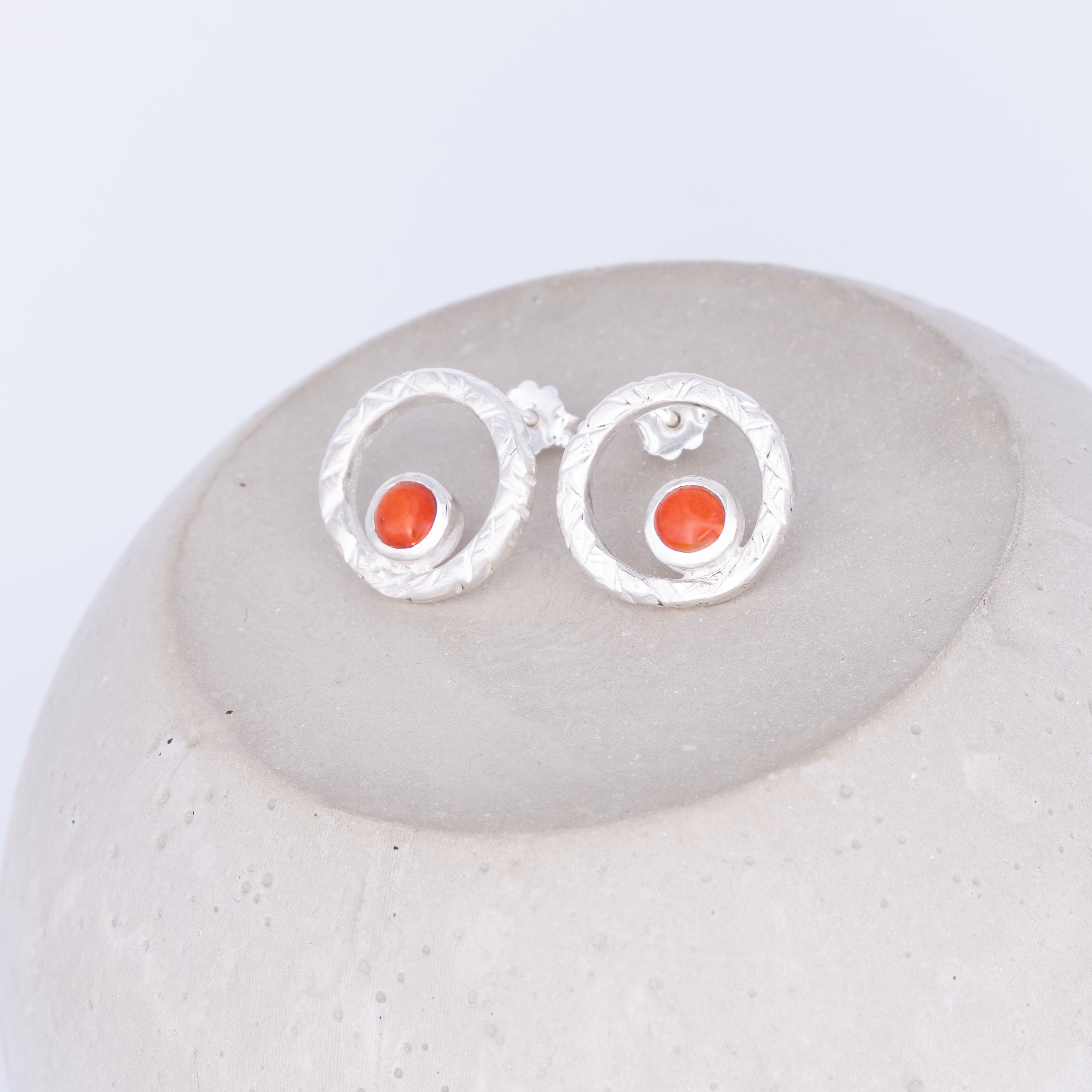 Silver earrings with orange stones on a white stone surface coral