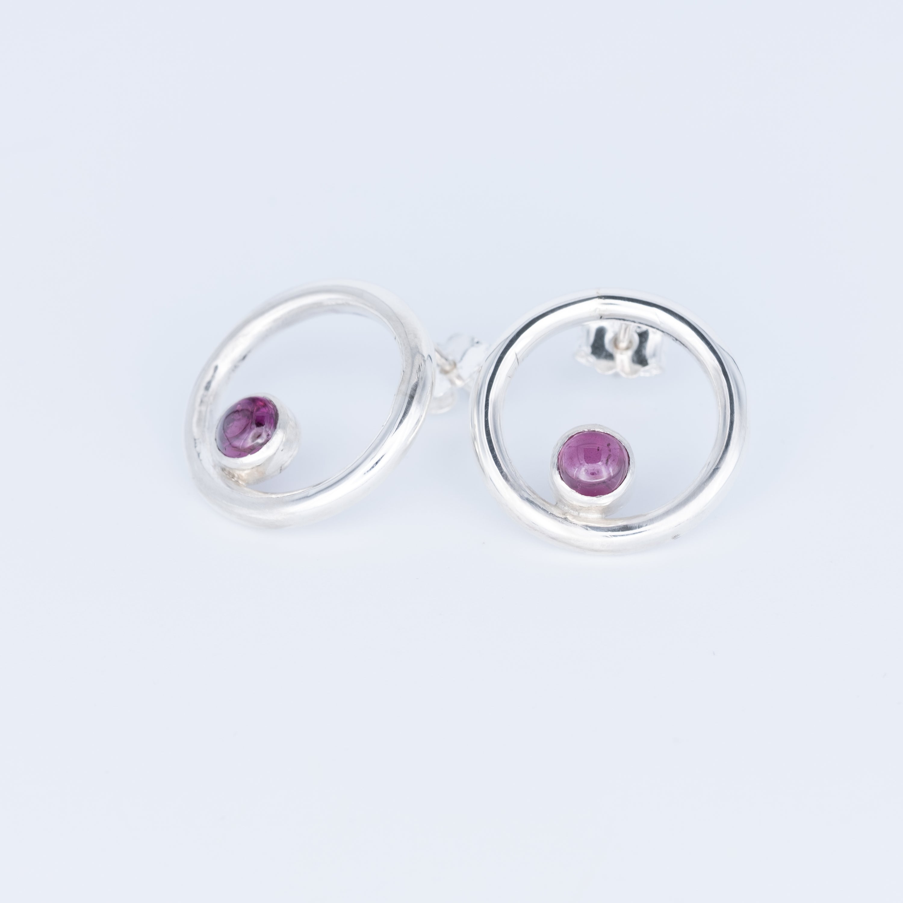 Silver earrings with purple gemstones on a light gray background