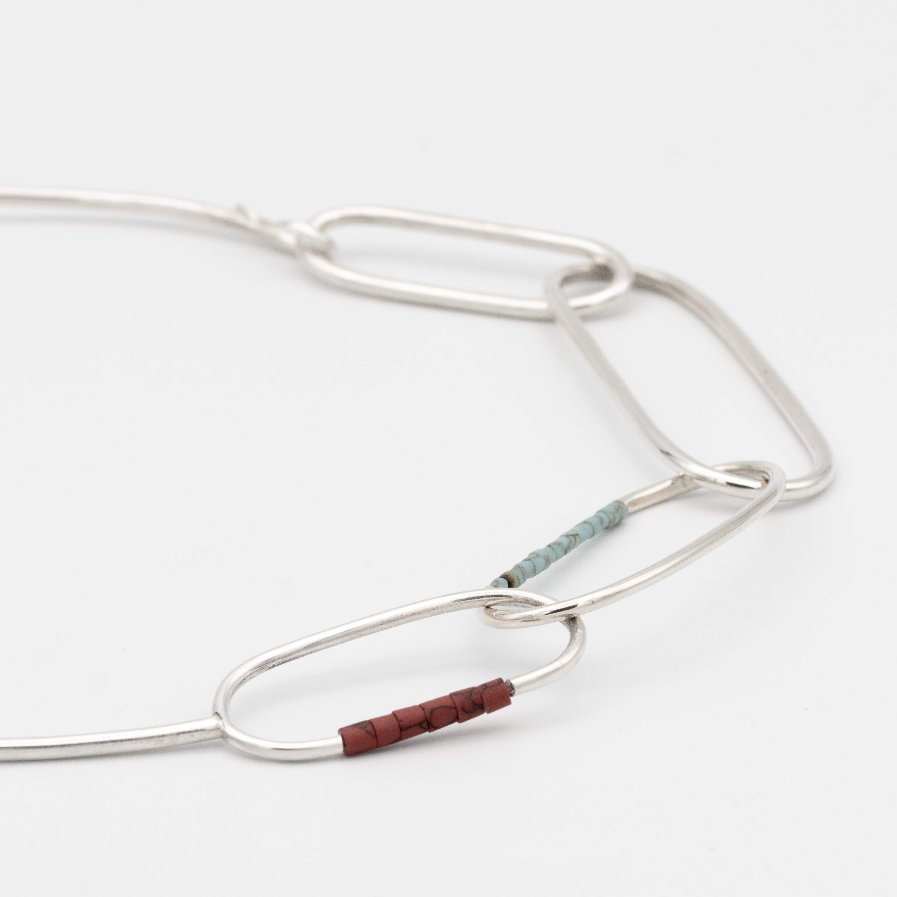 Silver necklace with a small brown bead on a white background