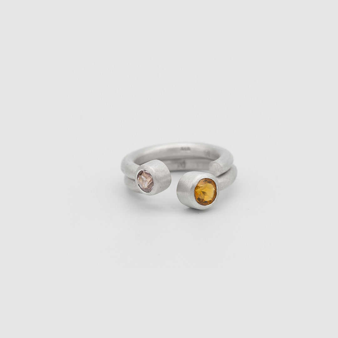 Silver ring with two round gemstones on a light gray background