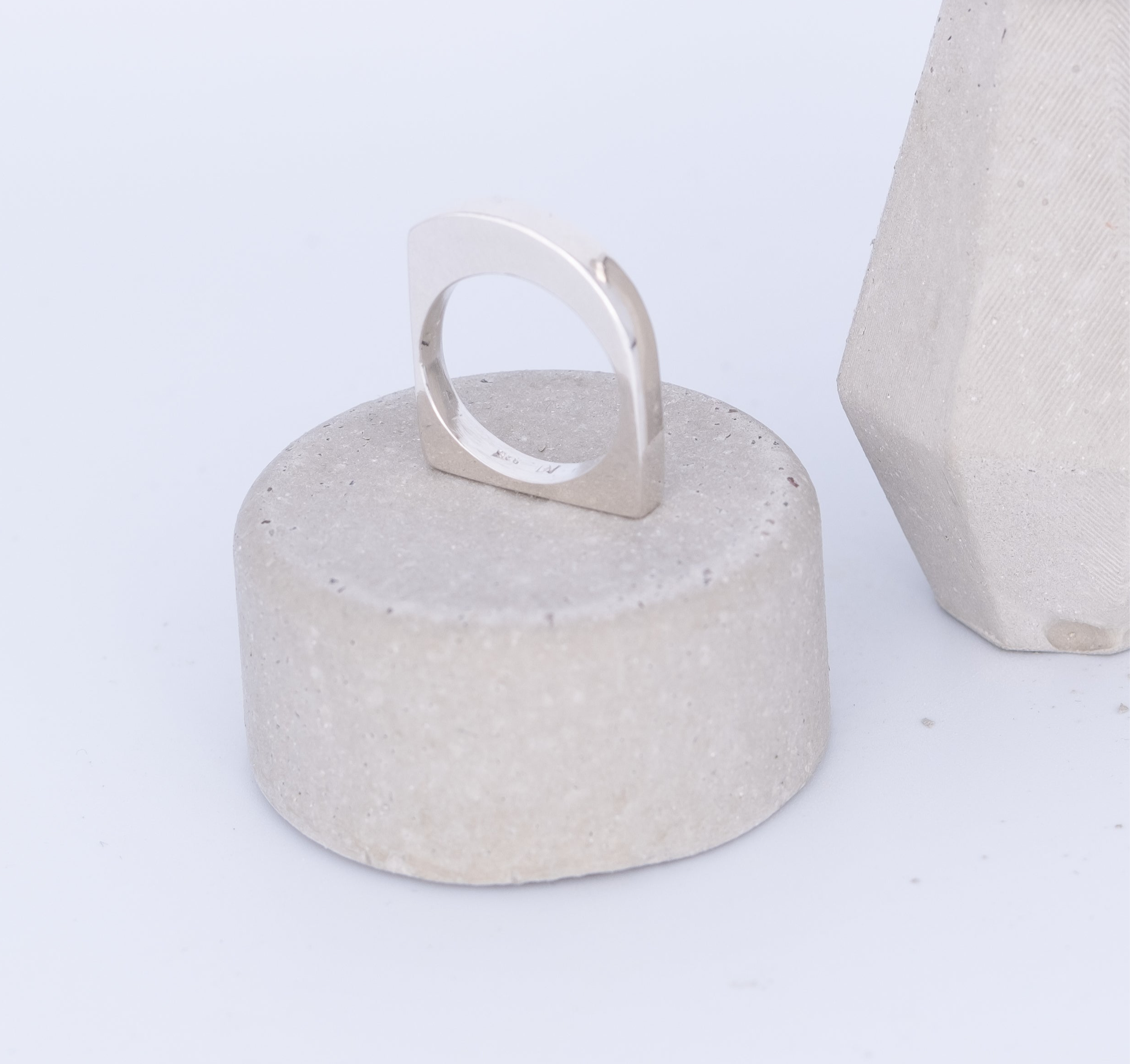 Silver ring on a textured concrete block with another similar block in the background.