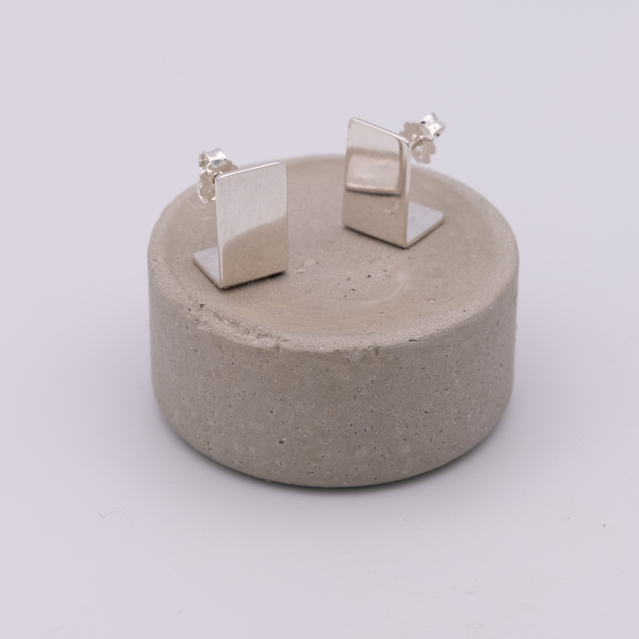 Pair of silver square earrings on a concrete stand against a white background