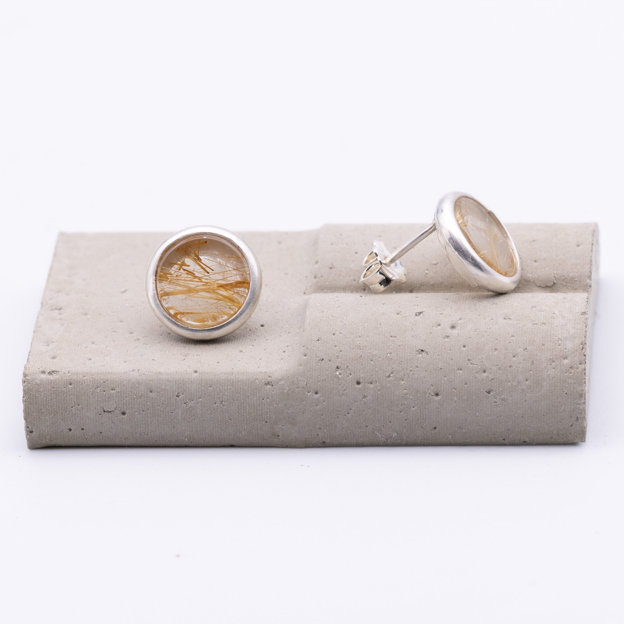 Silver earrings on a gray stone stand with a white background