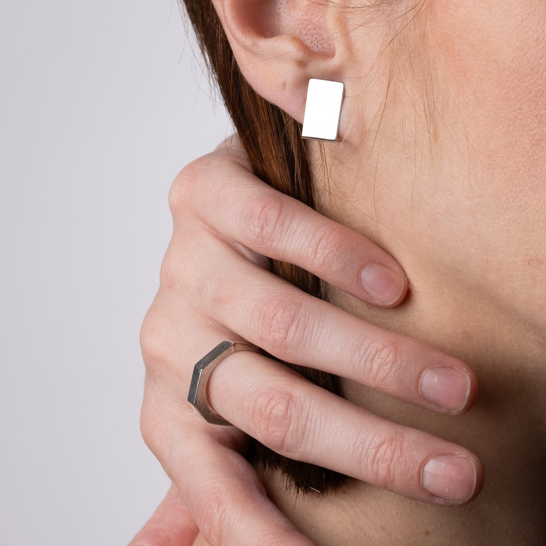 Close-up of a person wearing a silver hexagonal ring on a neutral background