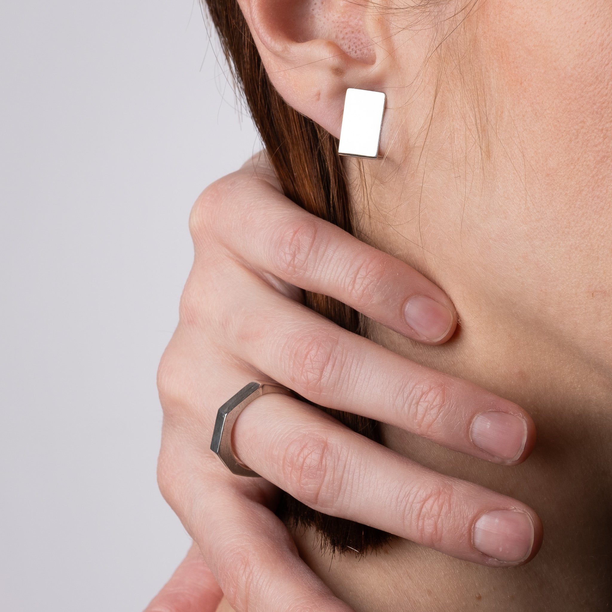 Close-up of a person wearing a silver hexagonal ring on a neutral background