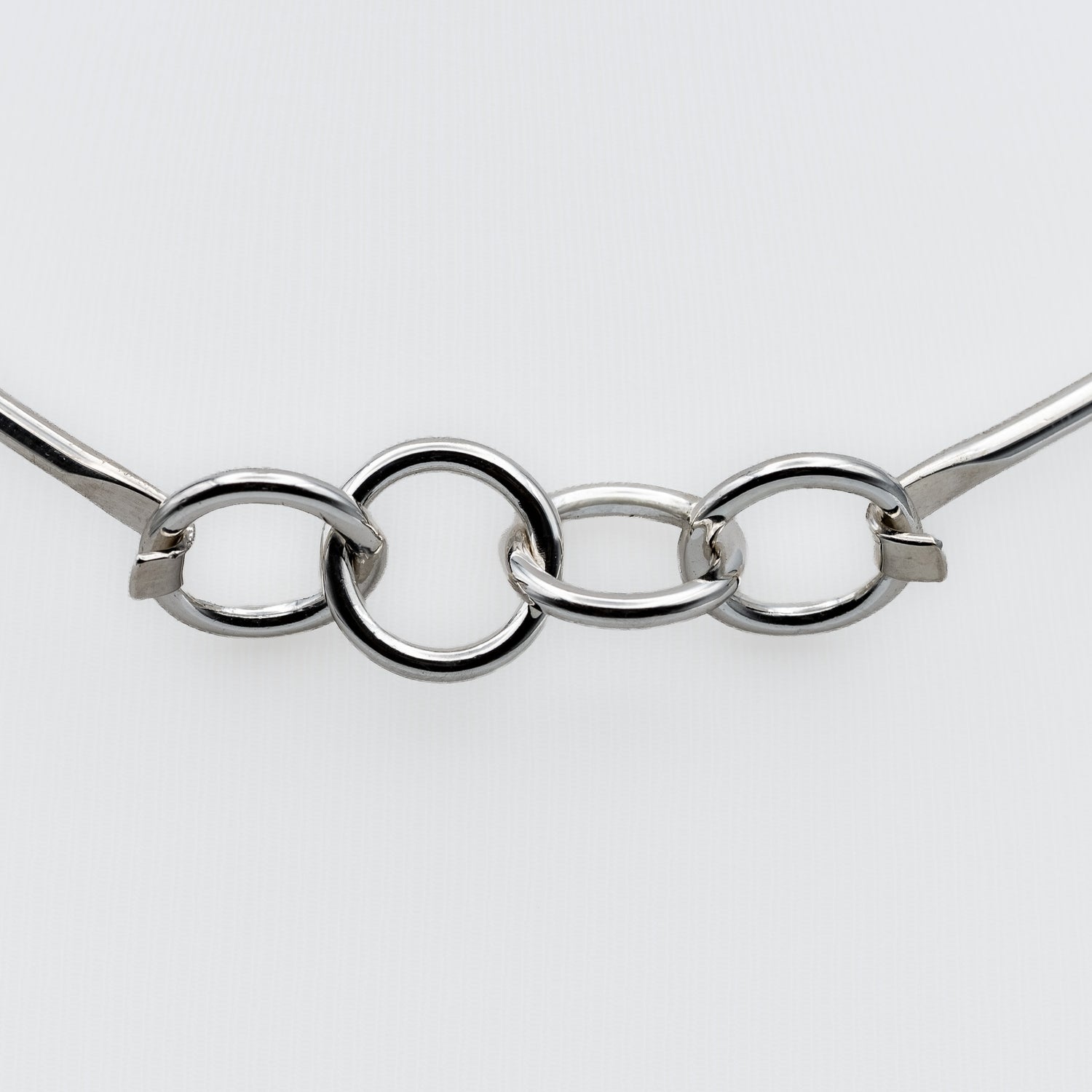 A close-up of a polished silver-tone metal chain with three interlocking oval links and small square connector pieces, shown against a plain light gray background.