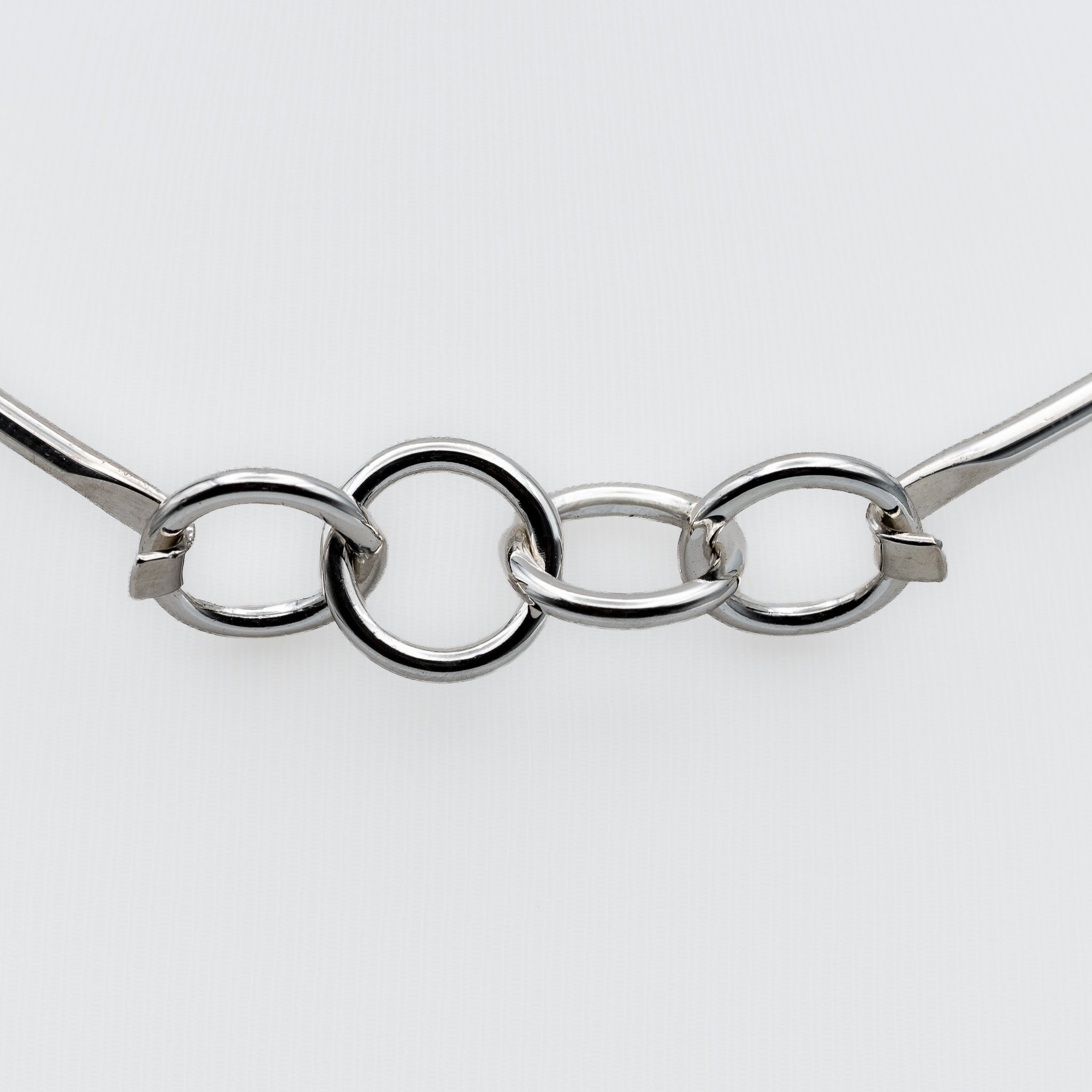 A close-up of a polished silver-tone metal chain with three interlocking oval links and small square connector pieces, shown against a plain light gray background.
