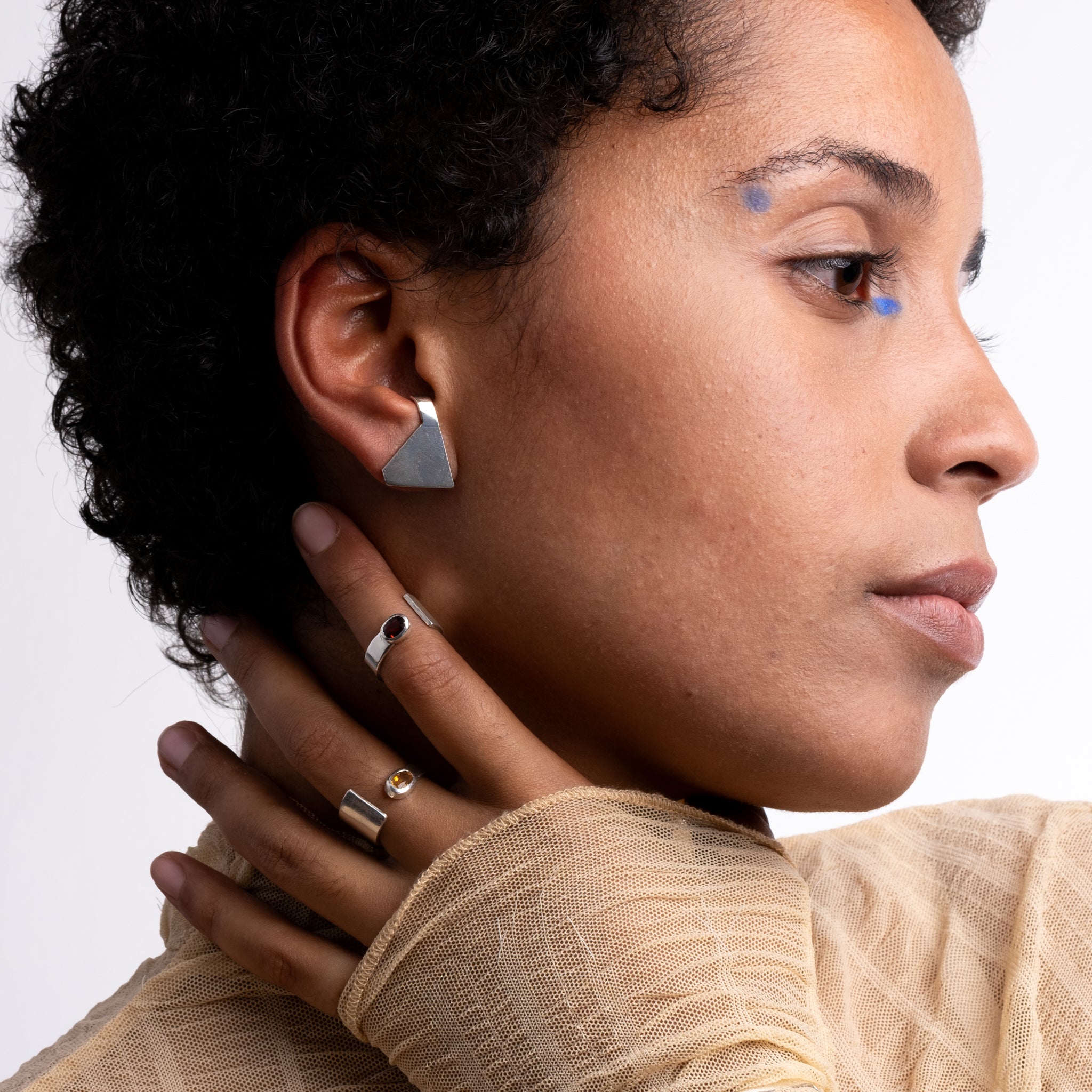Close-up of a woman wearing geometric earrings and rings on a neutral background