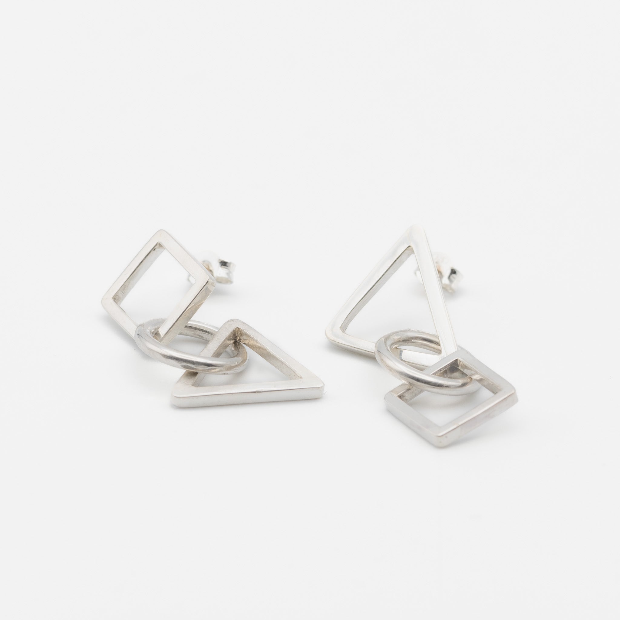 A pair of silver geometric dangle earrings featuring interlocking open triangles and squares, photographed on a clean white background.