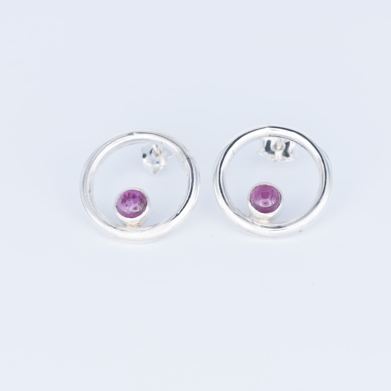 Silver earrings with pink gemstones on a light gray background