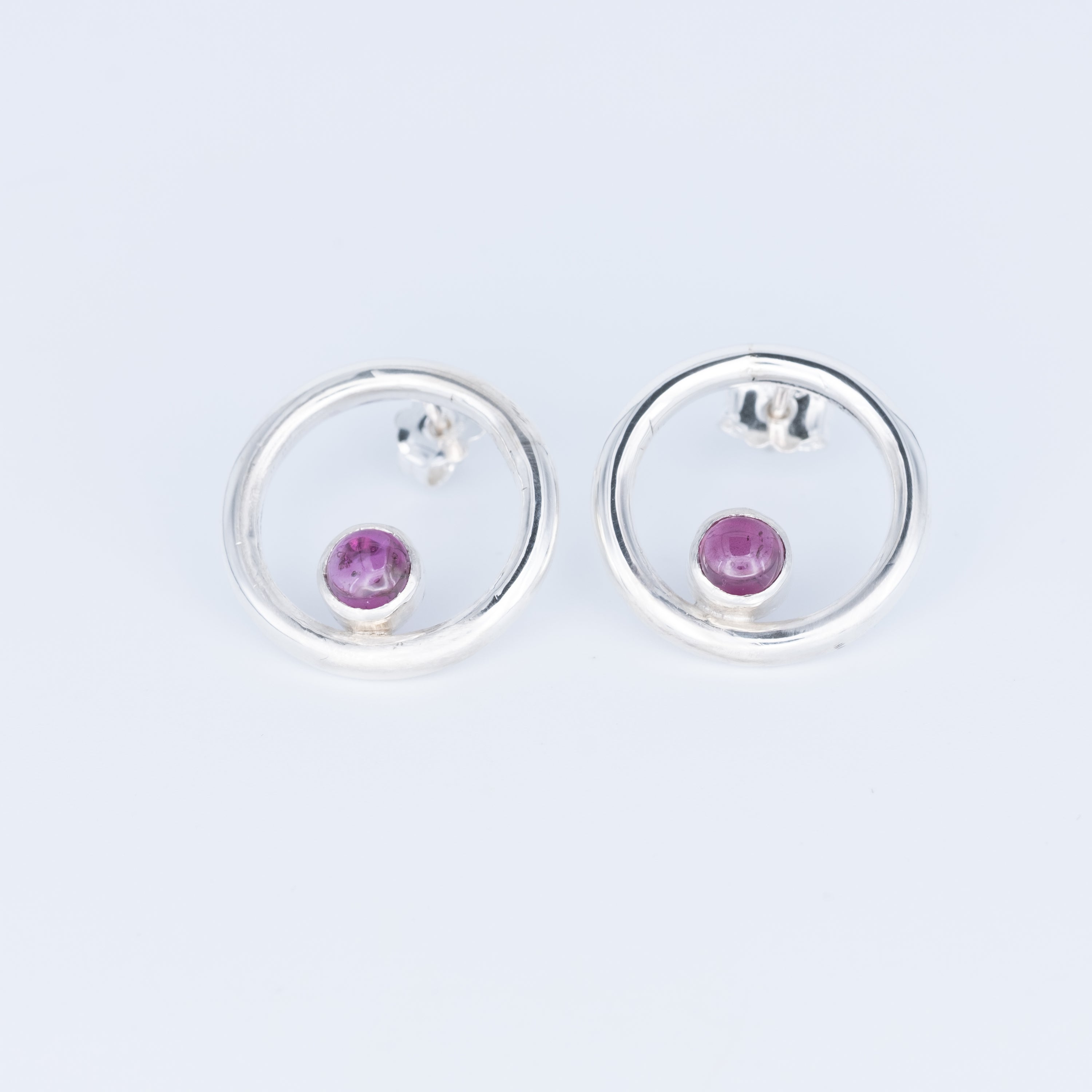Silver earrings with pink gemstones on a light gray background