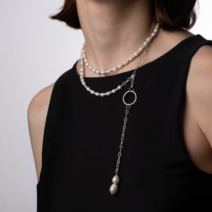 Pearl necklace with a pendant on a person wearing a black top against a plain background