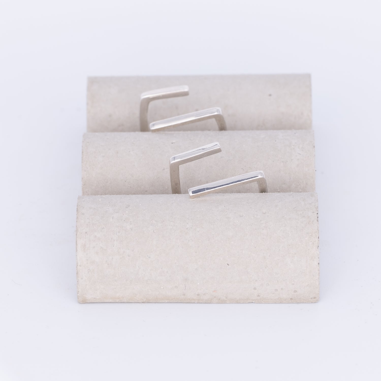 Set of silver earrings on a textured beige card against a white background