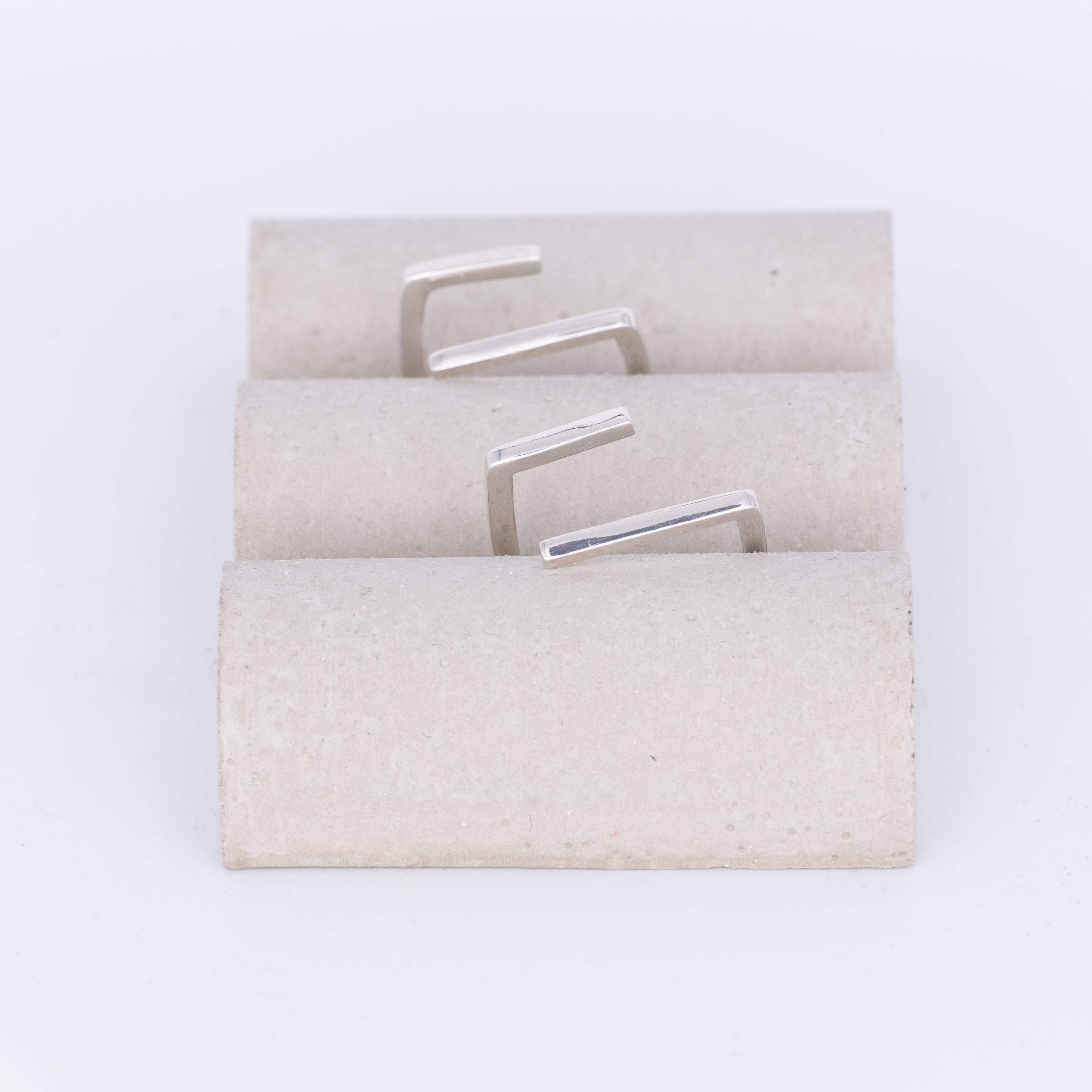 Set of silver earrings on a textured beige card against a white background