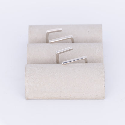 Set of silver earrings on a textured beige card against a white background
