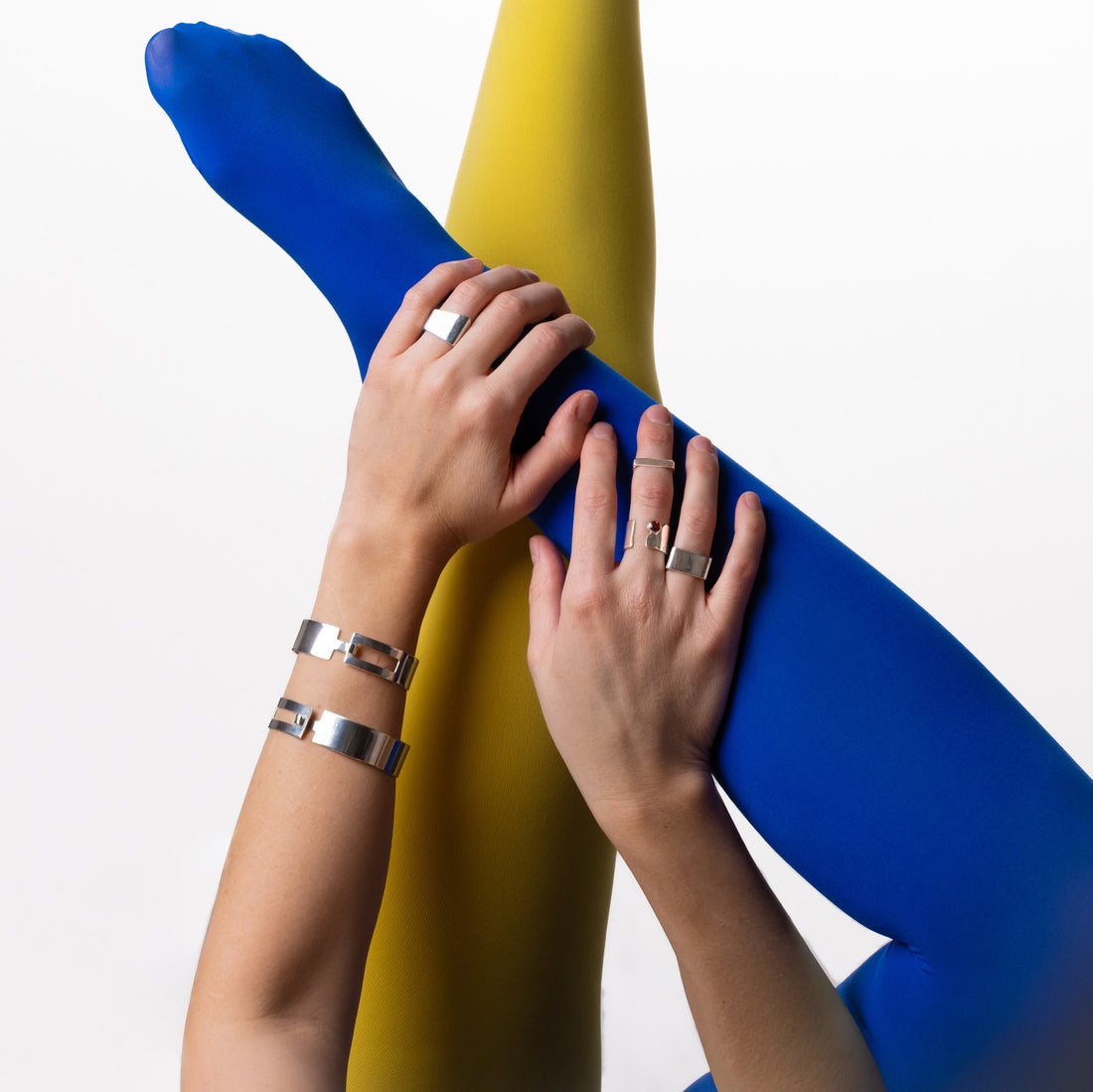 Two pairs of hands with rings and bracelets on a blue and yellow background