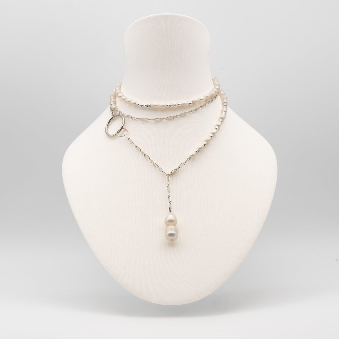 A layered silver-tone necklace displayed on a white mannequin bust. The necklace features a beaded choker layer, a delicate chain layer with a small silver ring accent, and a longer chain with a single white pearl pendant.