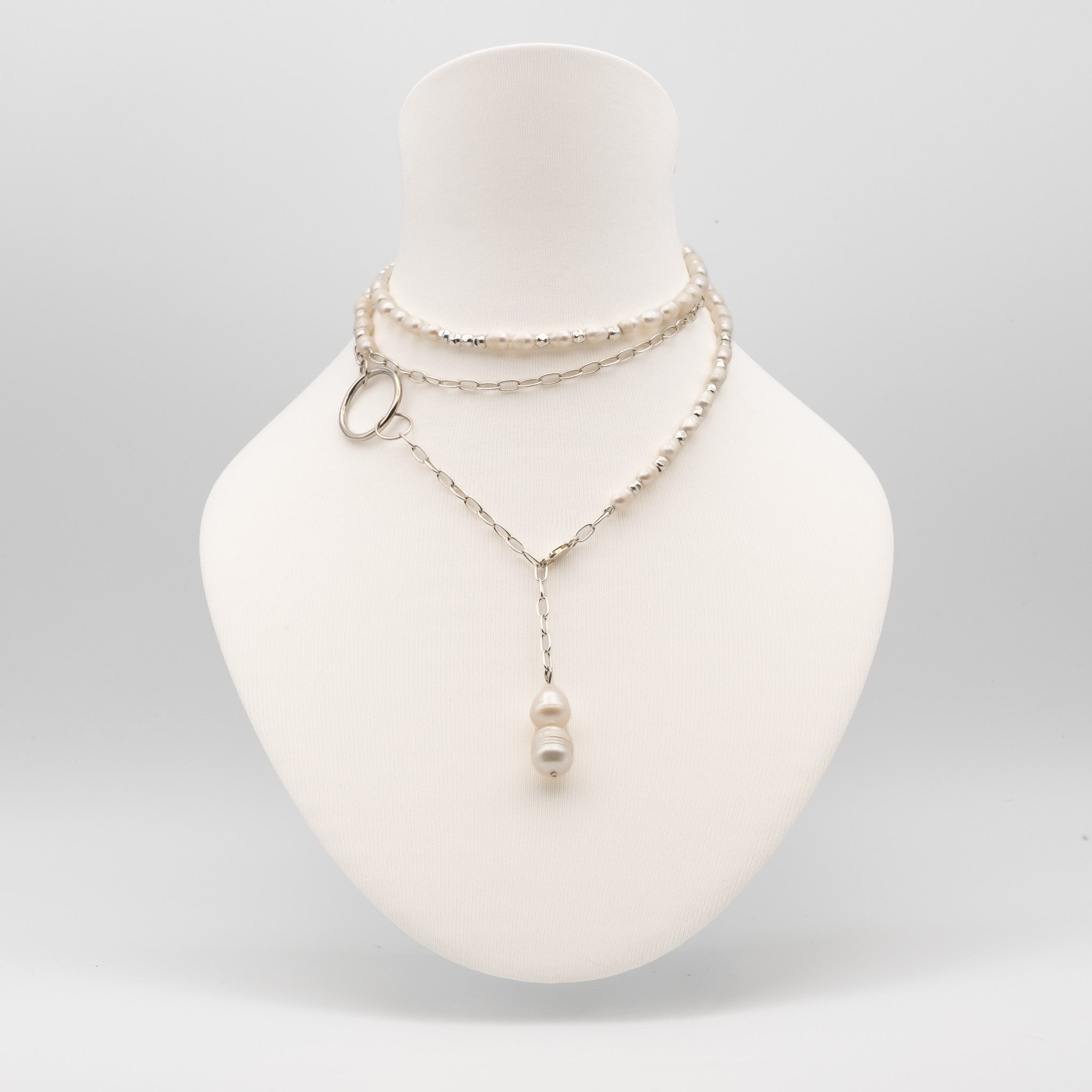 A layered silver-tone necklace displayed on a white mannequin bust. The necklace features a beaded choker layer, a delicate chain layer with a small silver ring accent, and a longer chain with a single white pearl pendant.
