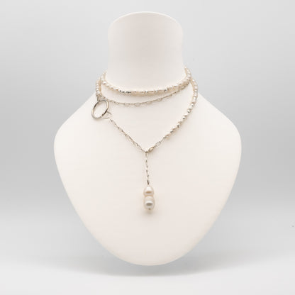 A layered silver-tone necklace displayed on a white mannequin bust. The necklace features a beaded choker layer, a delicate chain layer with a small silver ring accent, and a longer chain with a single white pearl pendant.