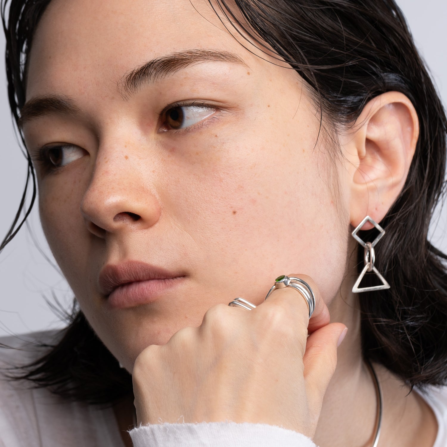 A close-up lifestyle shot of a model wearing a silver geometric dangle earring with a diamond and triangle design, along with silver rings.
