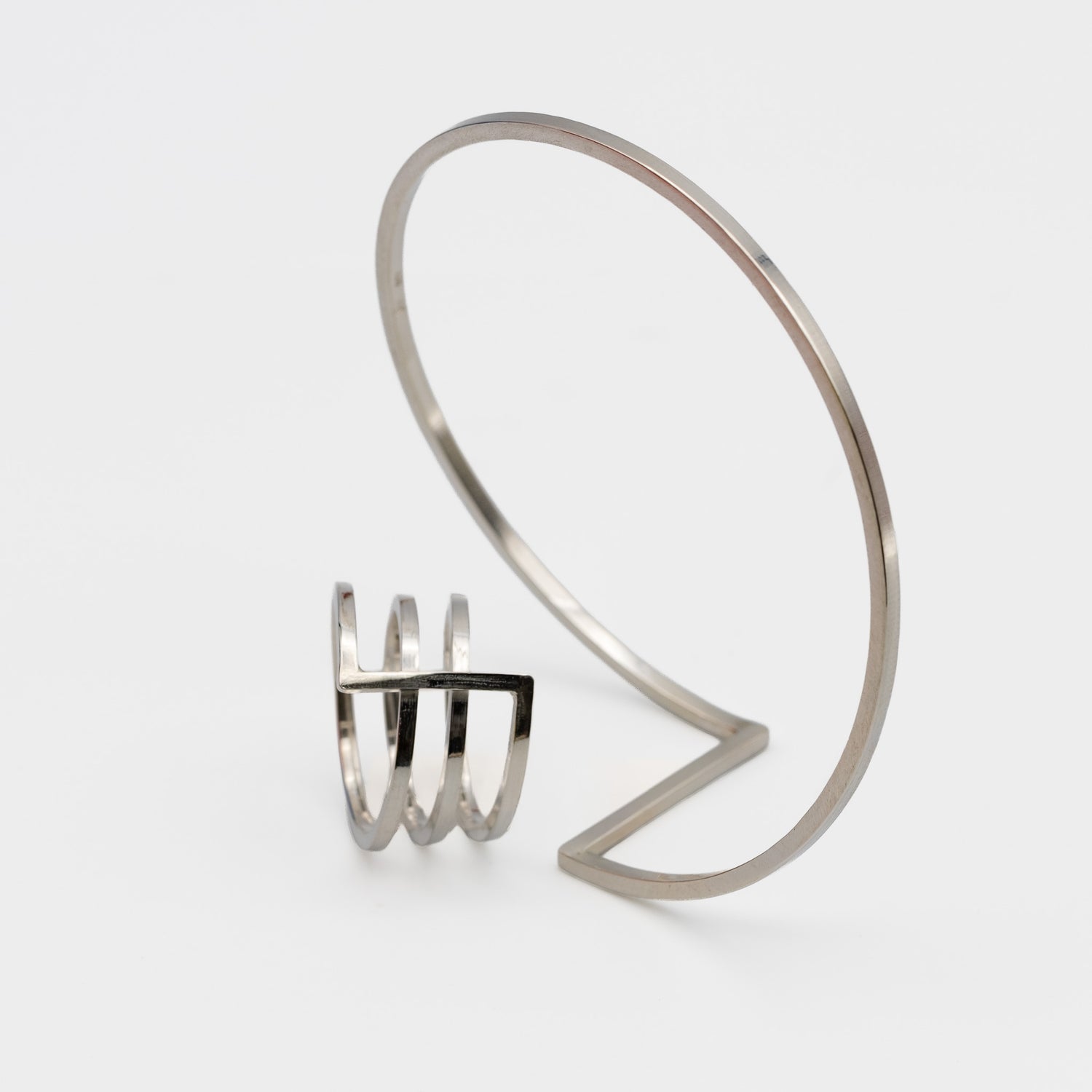A pair of minimalist silver jewerly. One ring and next to it one bangle-