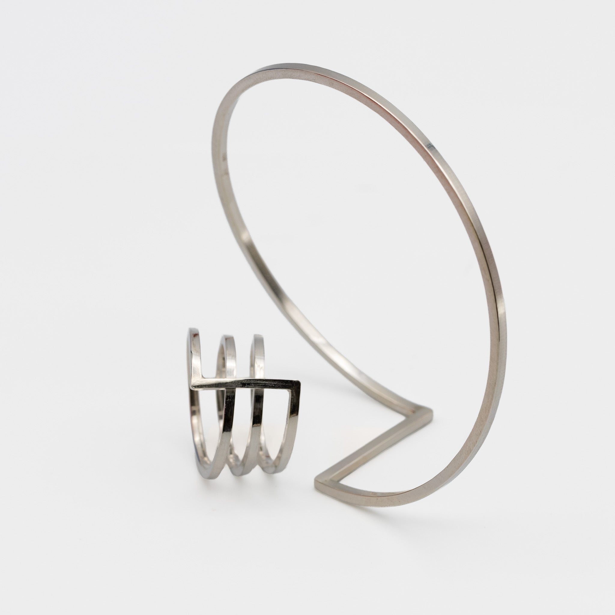 A pair of minimalist silver jewerly. One ring and next to it one bangle-