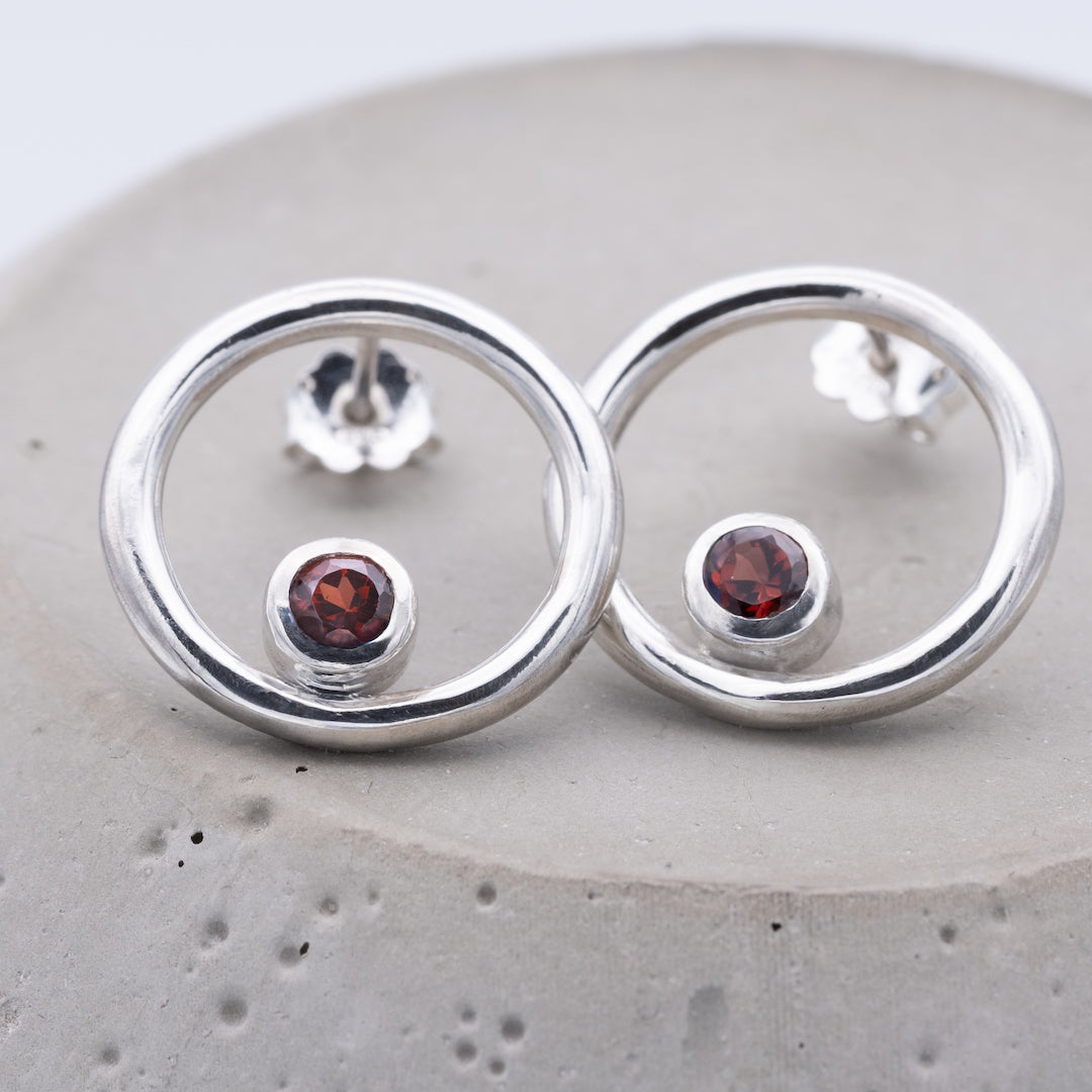 Silver earrings with red gemstones on a gray surface