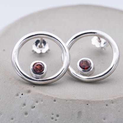 Silver earrings with red gemstones on a gray surface