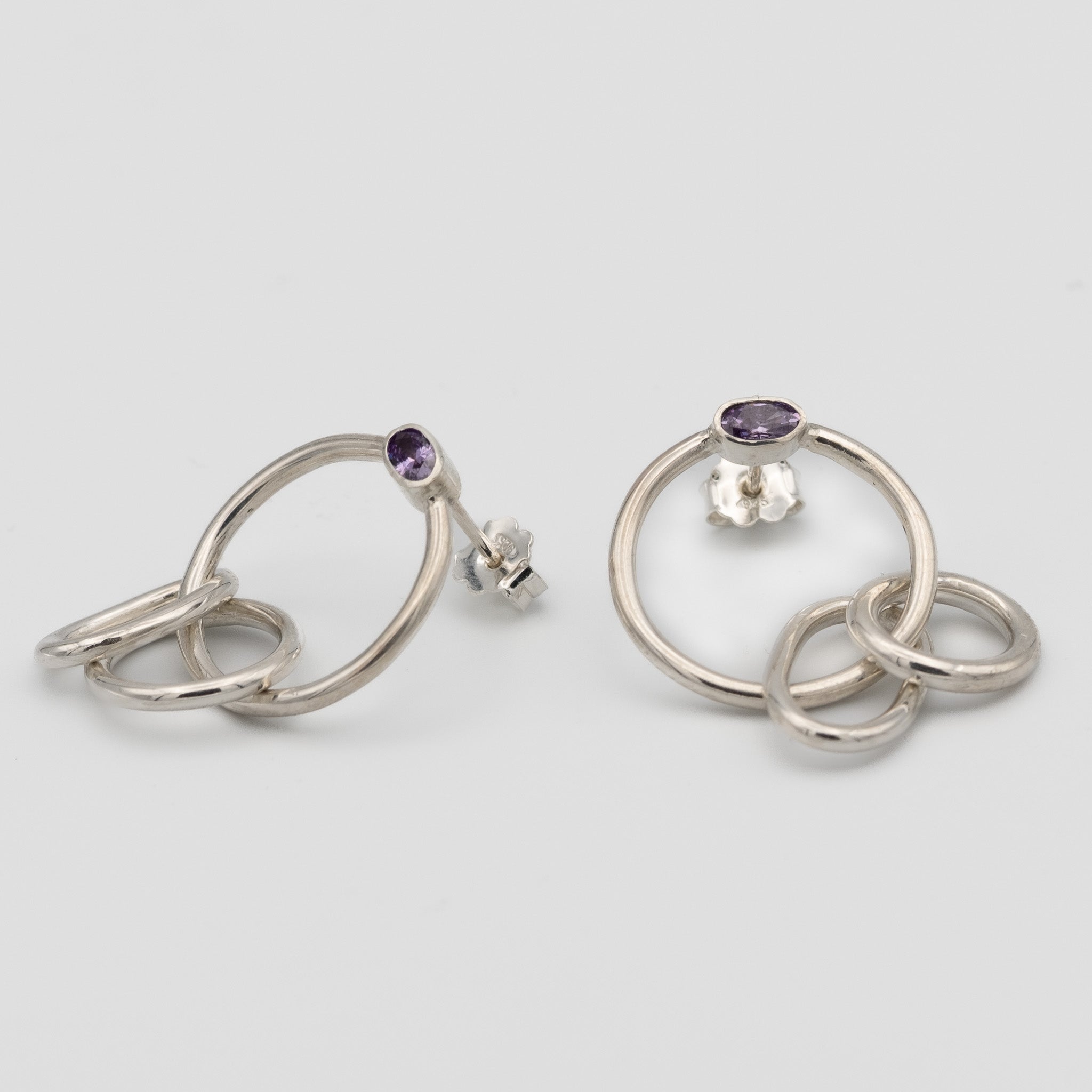 Silver hoop earrings with purple gemstones on a light gray background