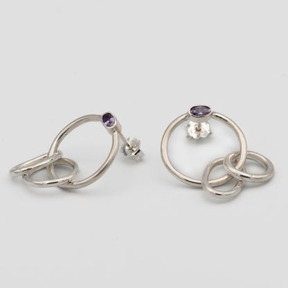 Silver hoop earrings with purple gemstones on a light gray background