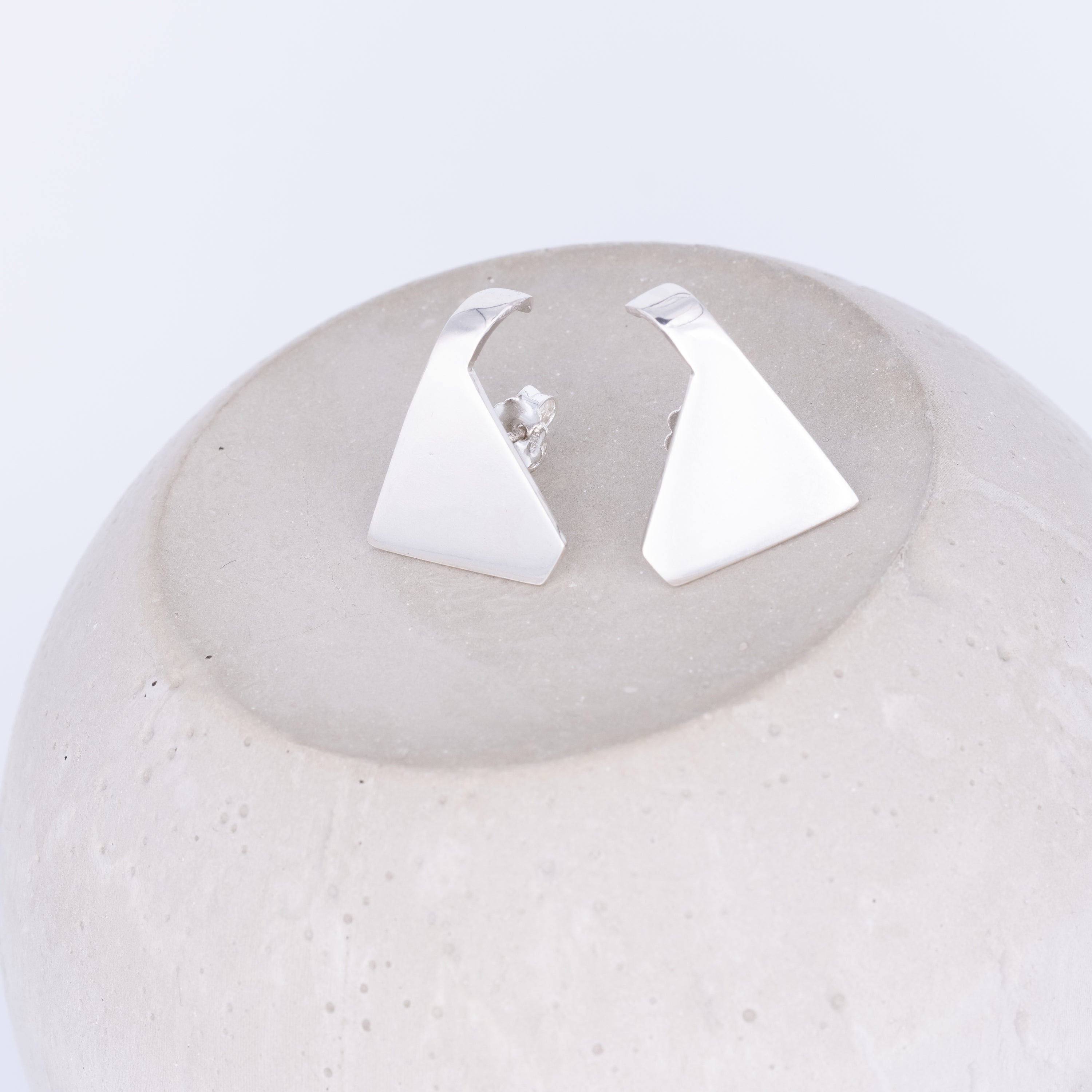 Pair of silver triangle earrings on a textured white surface