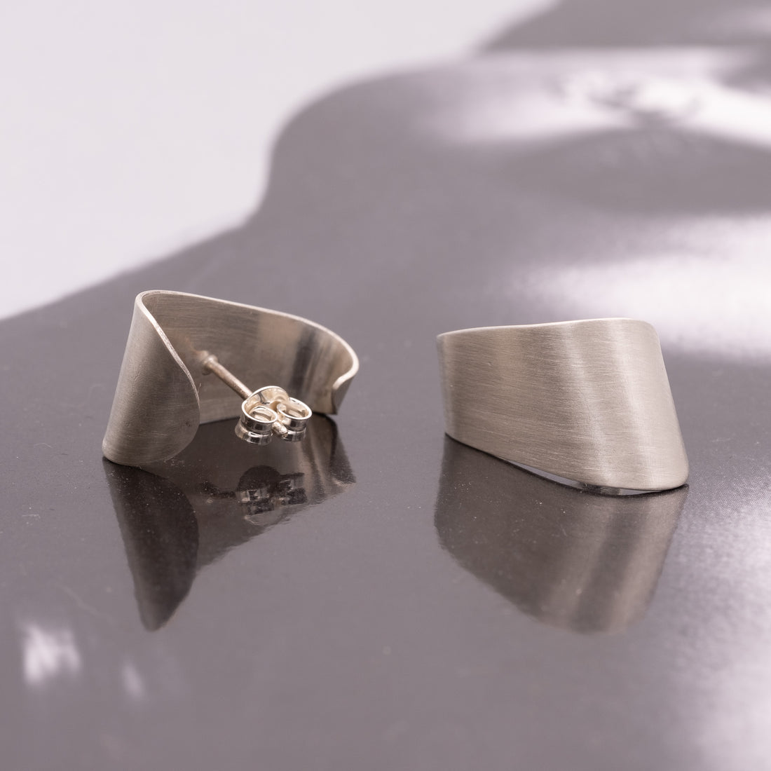 Pair of silver earrings on a reflective surface