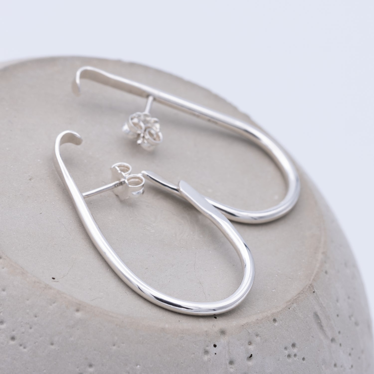 Silver hoop earrings on a textured stone surface