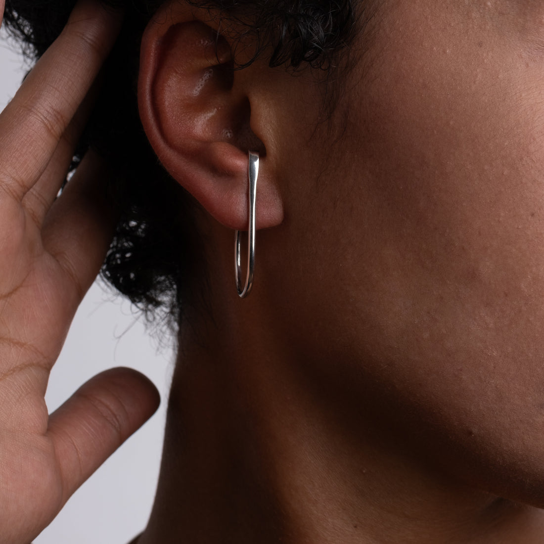 Close-up of an ear with a silver hoop earring against a neutral background