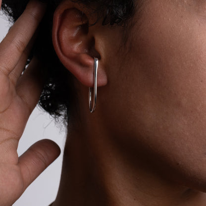 Close-up of an ear with a silver hoop earring against a neutral background