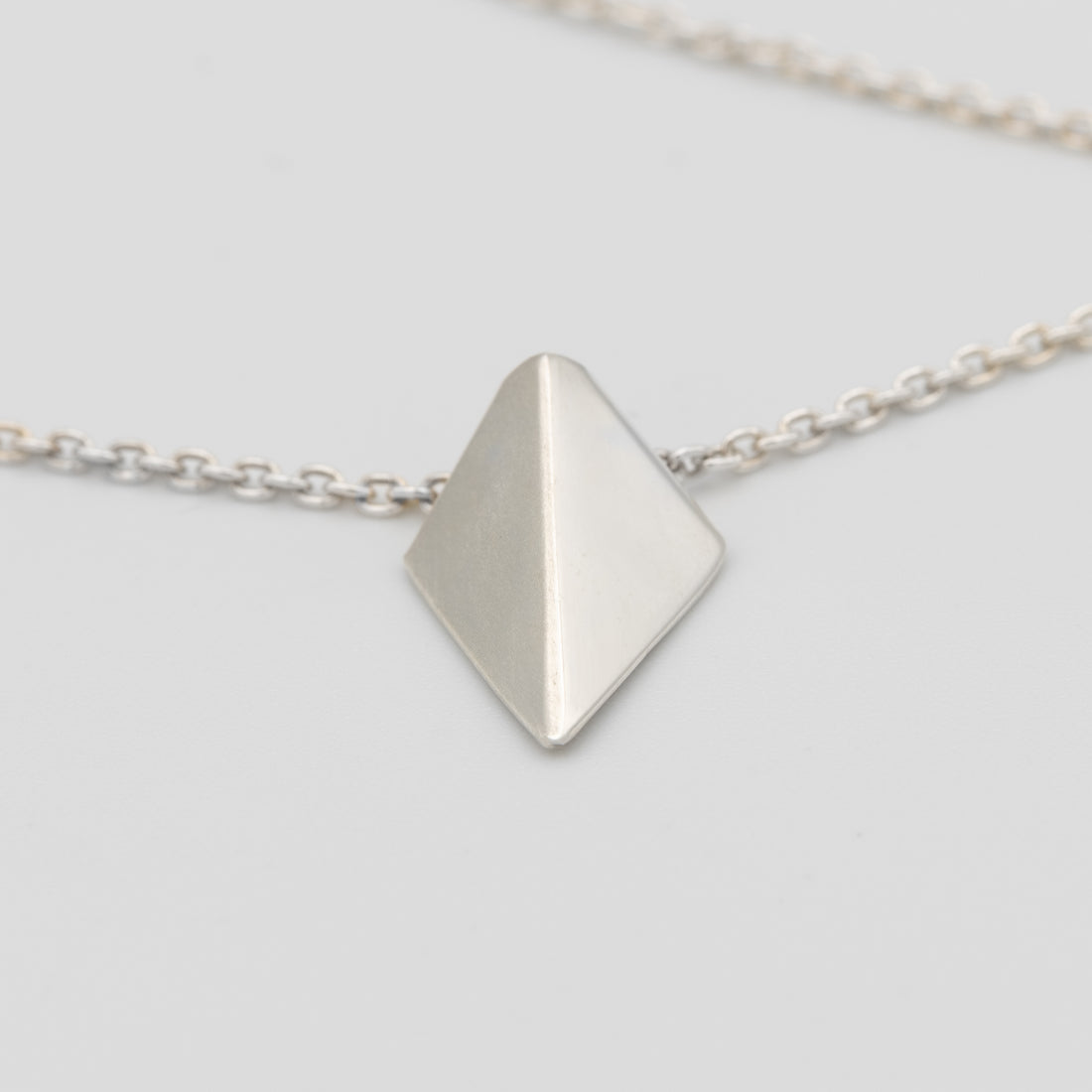 Silver necklace with a pyramid-shaped pendant on a light gray background