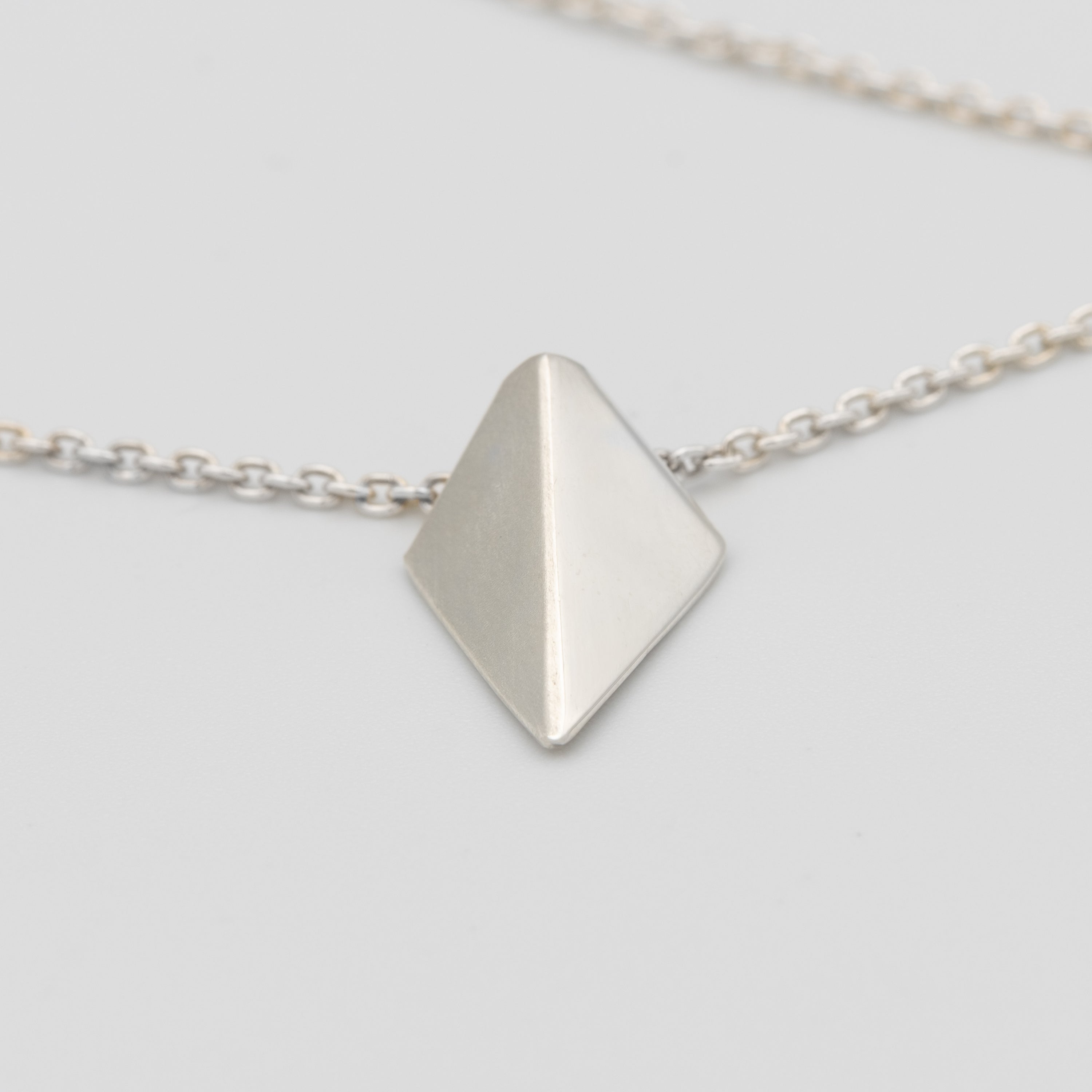 Silver necklace with a pyramid-shaped pendant on a light gray background