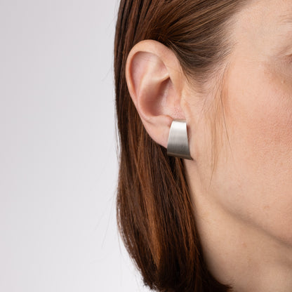 Close-up of a person wearing a silver hoop earring on a plain background