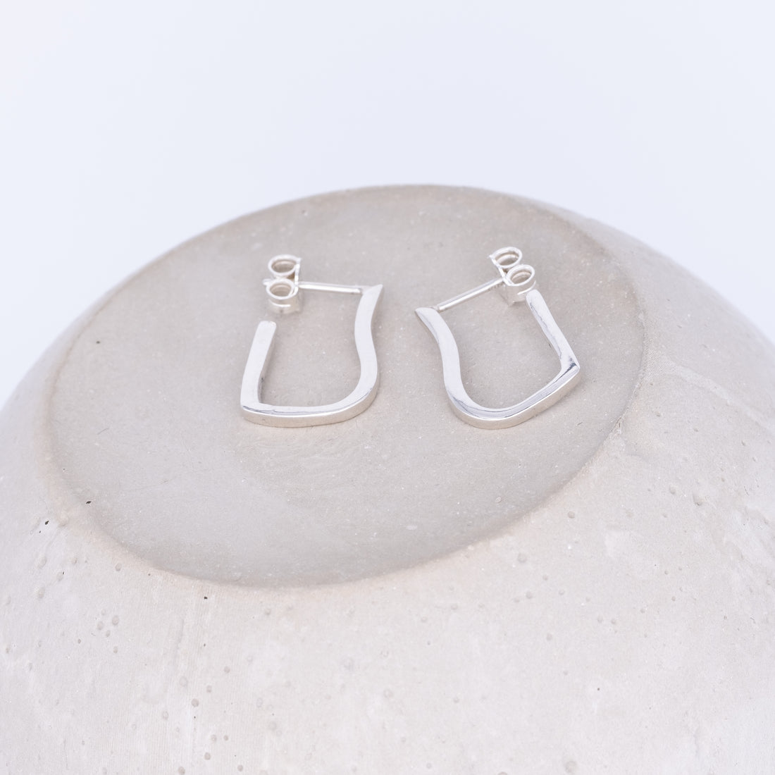 Silver hoop earrings on a round stone surface