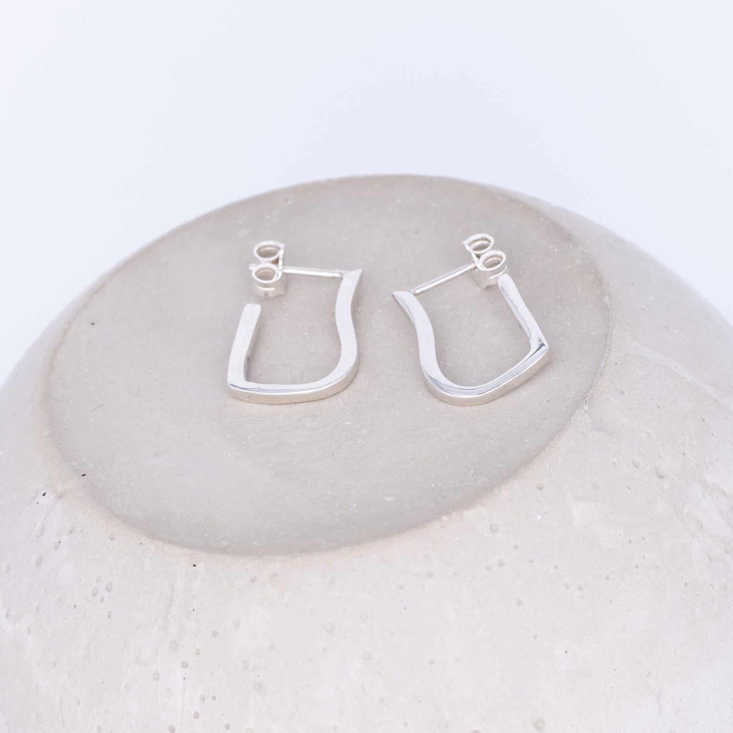 Silver hoop earrings on a round stone surface