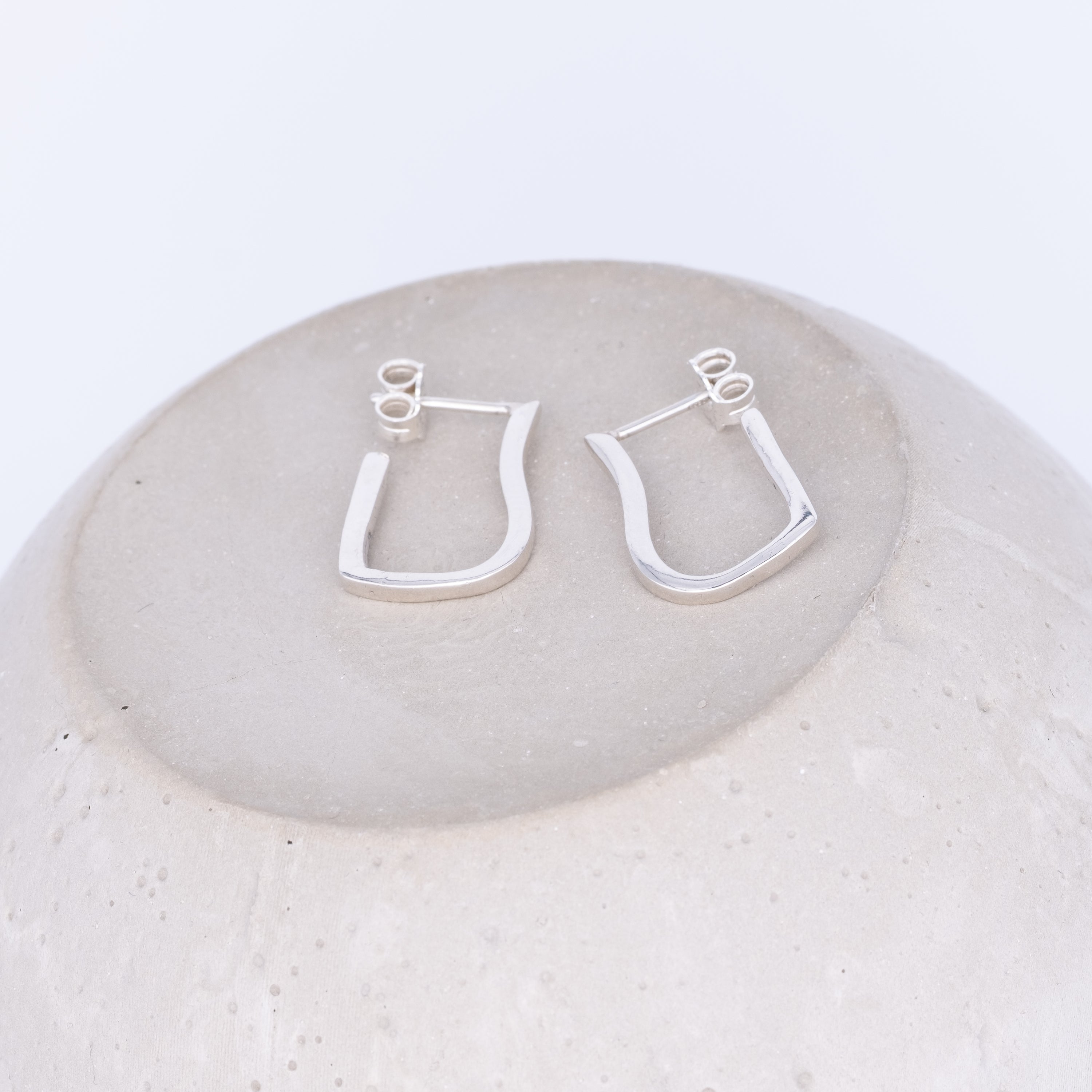 Silver hoop earrings on a round stone surface