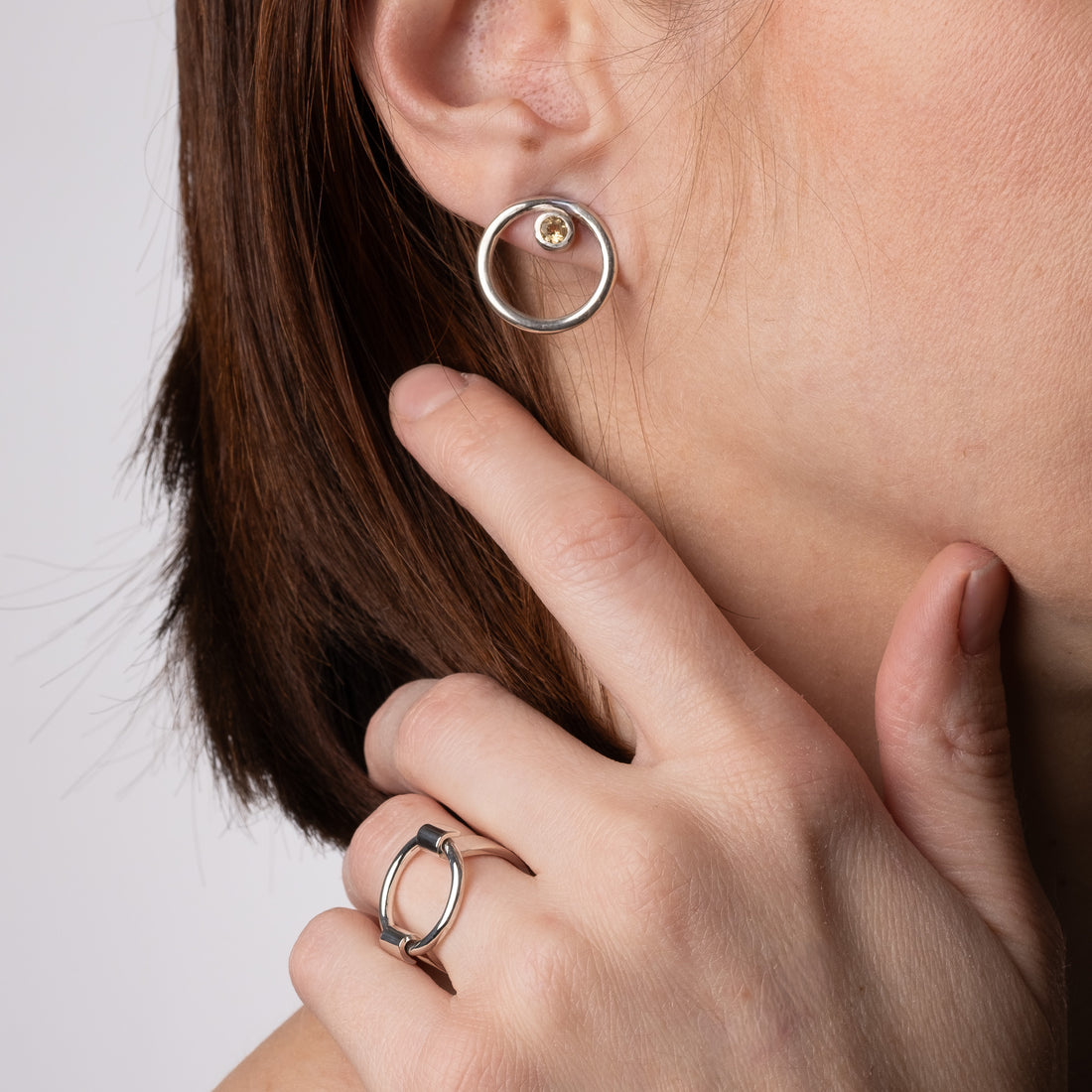 Close-up of a person wearing a silver hoop earring and matching ring on a neutral background