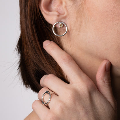 Close-up of a person wearing a silver hoop earring and matching ring on a neutral background