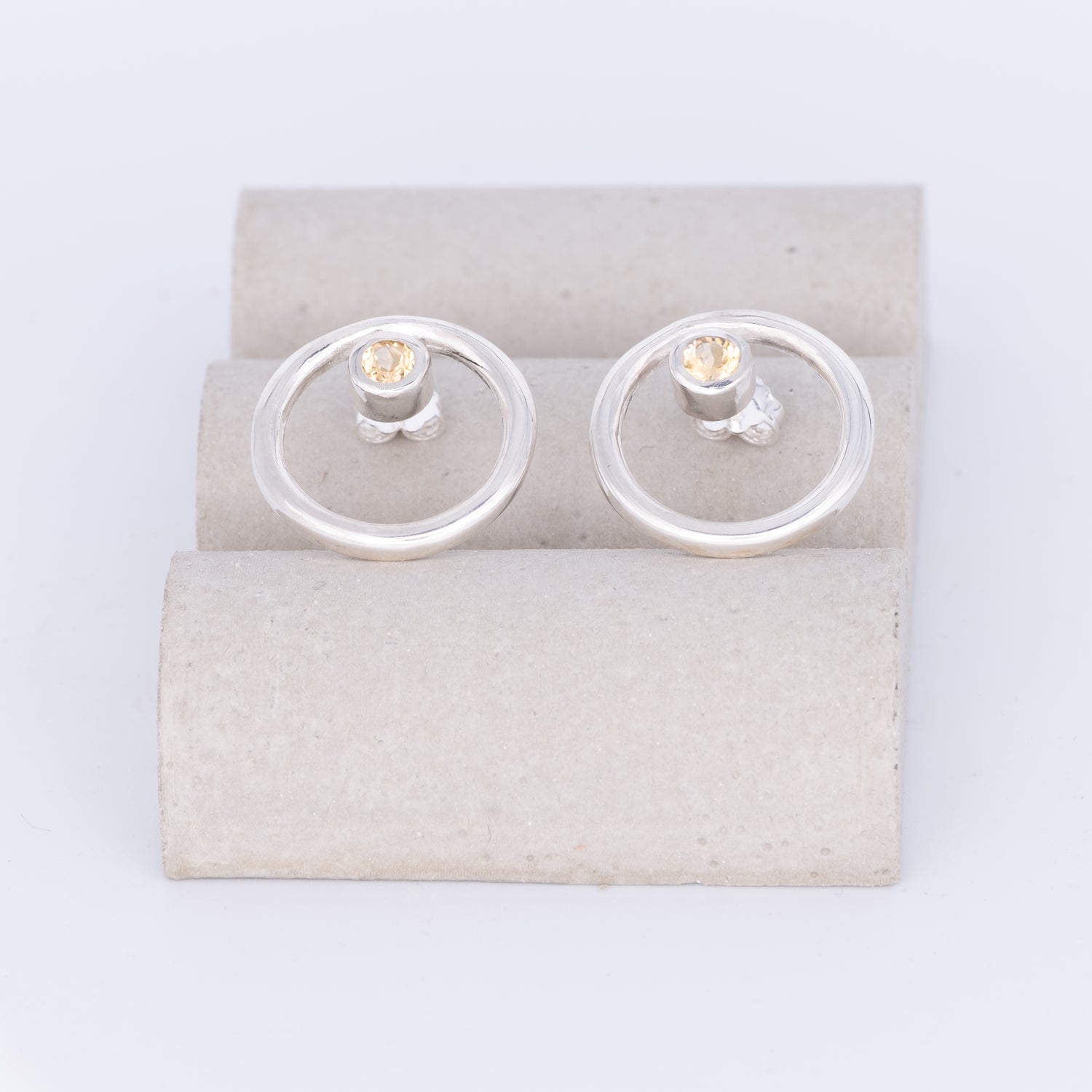 Silver earrings with clear gemstones on a beige card against a white background